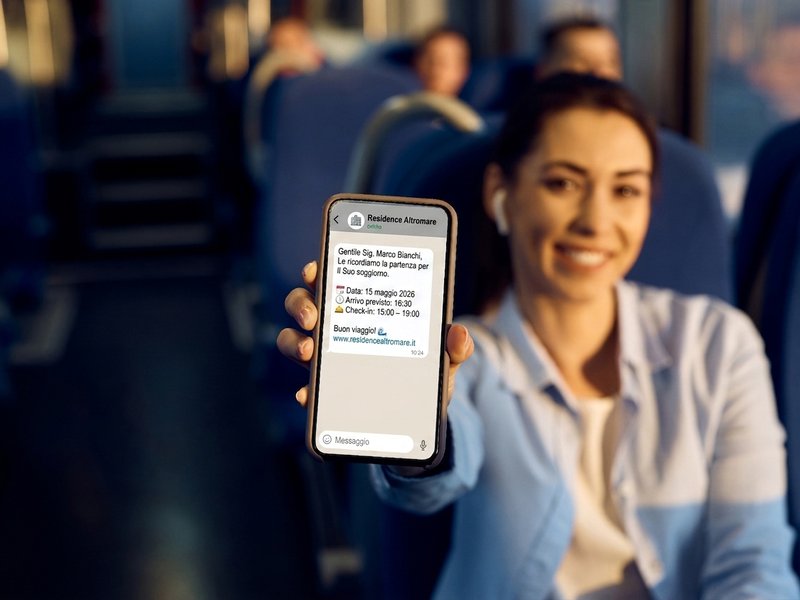 Cliente in viaggio in treno mostra sullo smartphone il promemoria di partenza WhatsApp inviato dal Residence Altromare con Kollego® WhatsApp Travel
